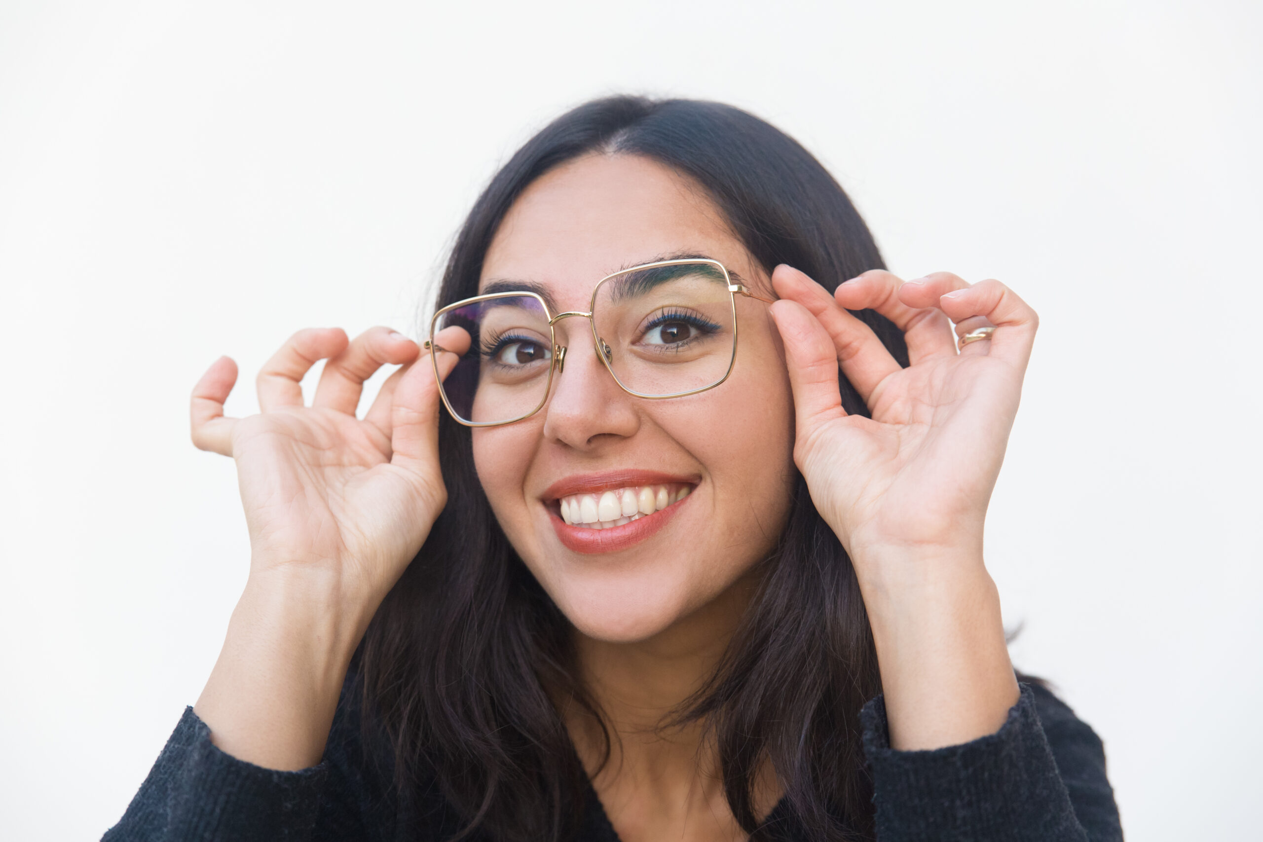 Closeup of happy joyful woman adjusting glasses, looking at camera, smiling. Beautiful young woman in casual sweater posing isolated over white background. Eyewear concept